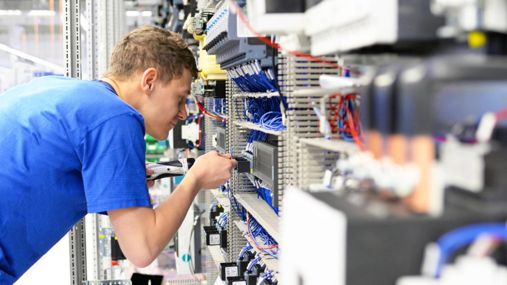 Ein junger Elektriker in blauem Shirt arbeitet an einem Verteilerschrank