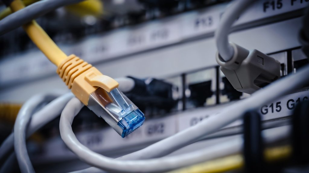 Nahaufnahme eines gelben Ethernet-Kabels, das in einen Netzwerk-Switch eingesteckt ist, umgeben von mehreren grauen Kabeln
