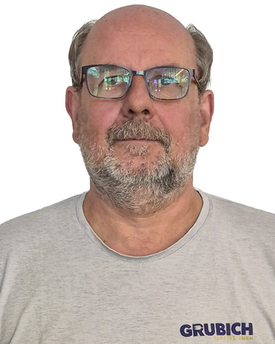 Oberkörper eines Mannes mit grauem T-Shirt, auf dem rechts unten der Schriftzug 'GRUBICH' in Großbuchstaben zu sehen ist